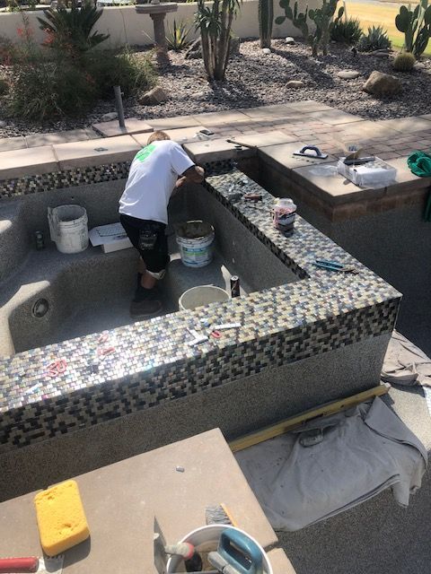 Person cleaning a mosaic-tiled outdoor fountain with buckets and tools in a desert courtyard