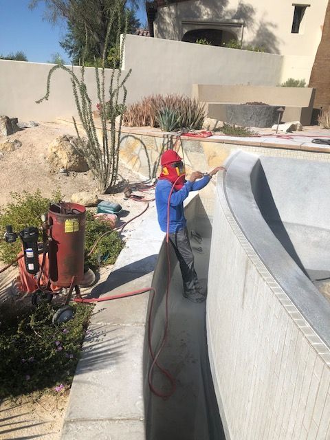 Worker in blue and red spraying a white pool wall with a hose in a sunny outdoor yard