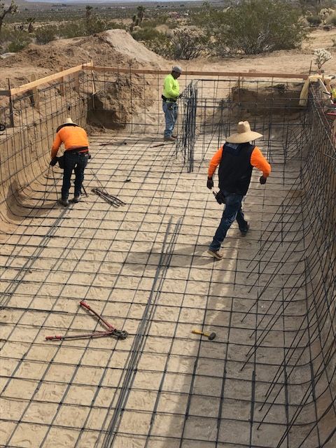 Workers installing rebar on a concrete foundation at a construction site in a desert landscape