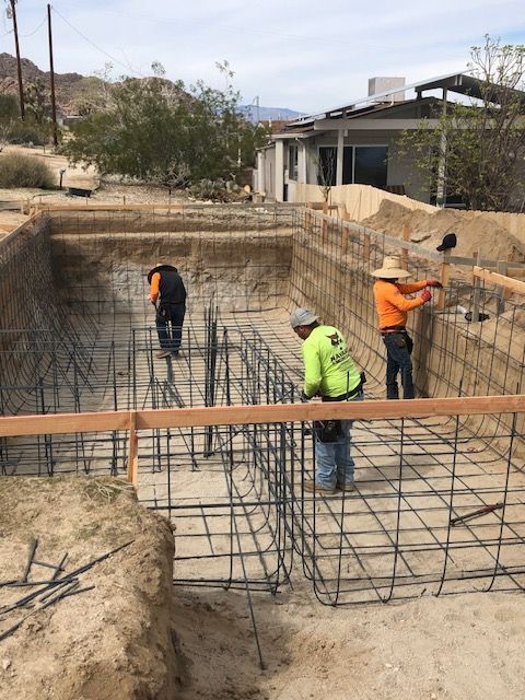 Workers installing rebar in a foundation excavation at a construction site