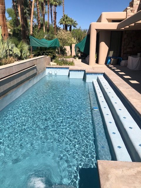 Backyard pool with blue water, steps, and desert landscaping beside a shaded patio