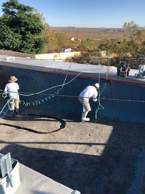 Two workers on a rooftop beside a blue wall, handling ropes under a clear sky.