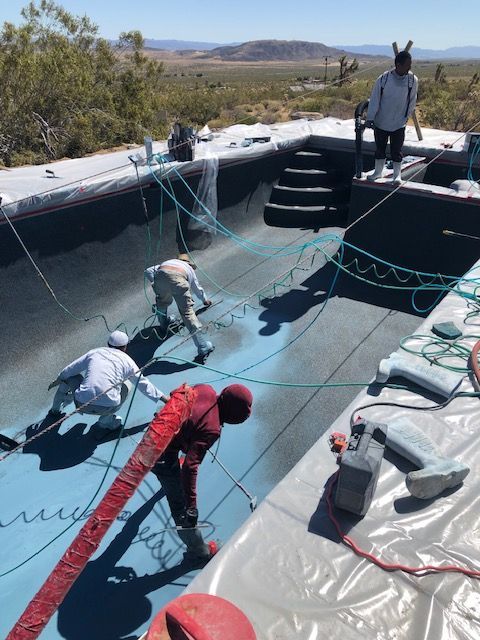 Workers coating a large concrete basin with blue waterproof sealant outdoors in a dry landscape