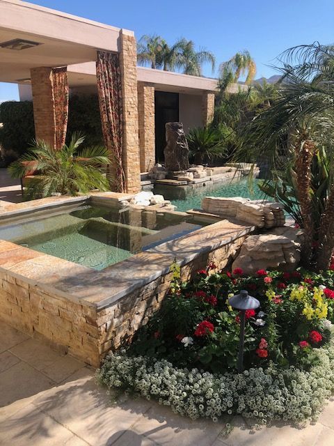 Luxury courtyard with stone fountain, pool, tropical plants, and colorful flowers under a shaded patio.