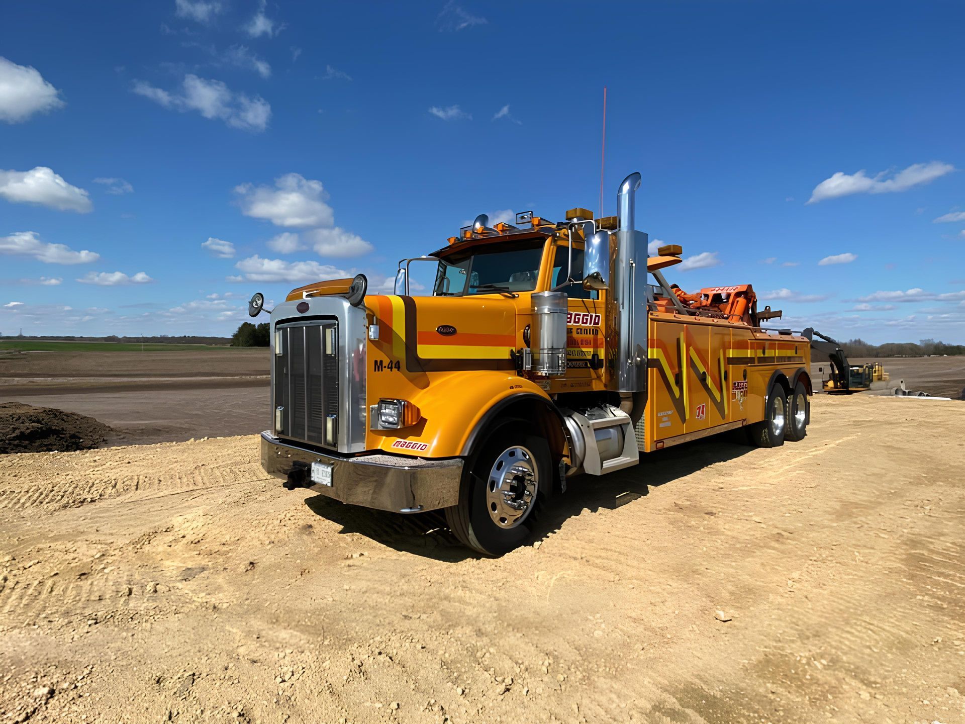 Yellow tow truck on dirt road under blue sky.