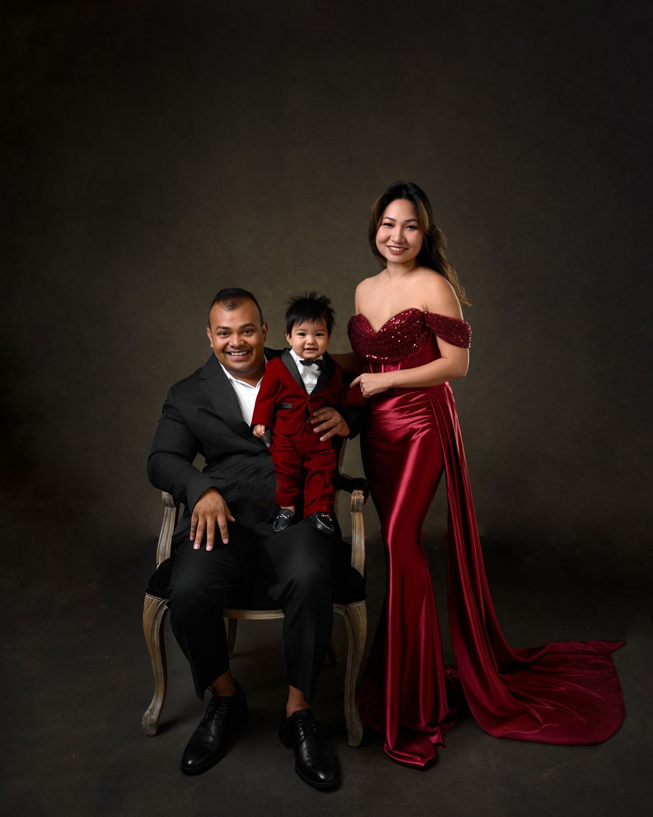 Studio portrait of three people in formal red and black attire on a dark backdrop.
