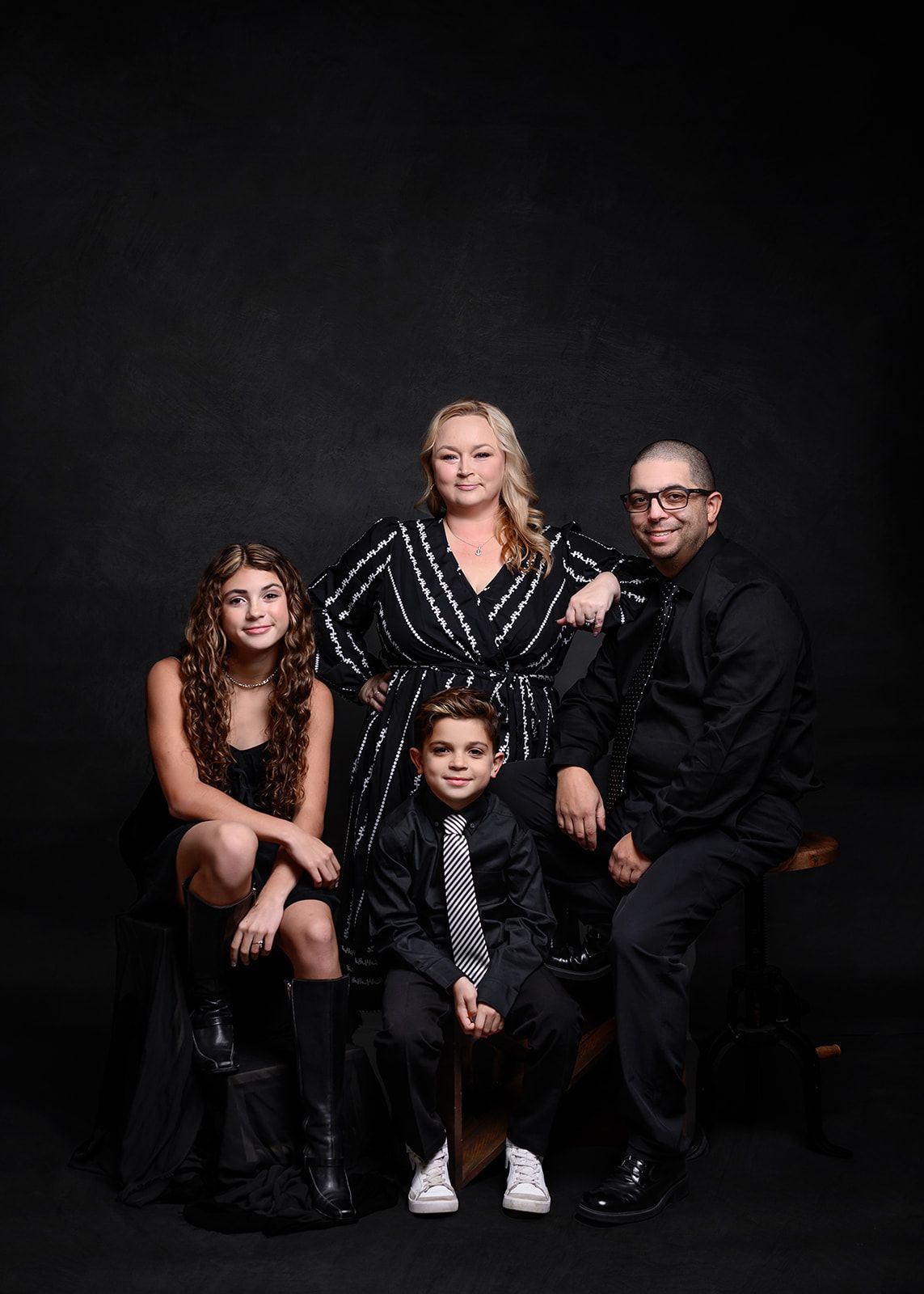 Formal family portrait of four people seated and standing against a dark studio backdrop.