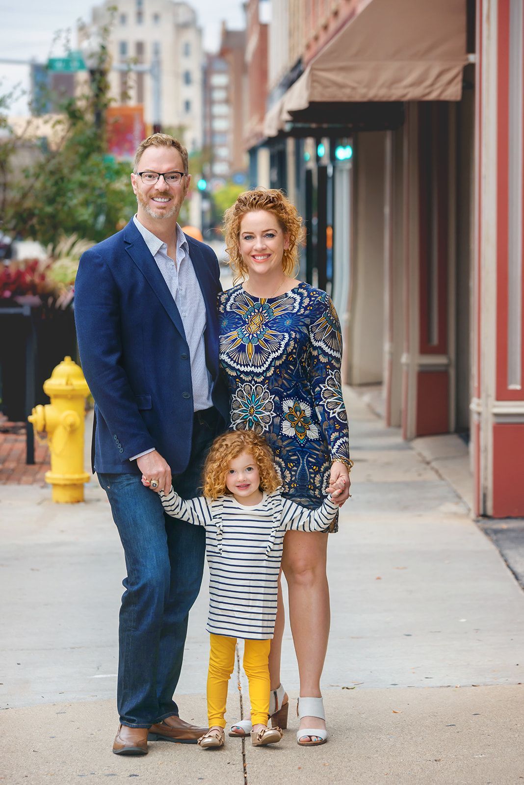 Three people standing on a city sidewalk, with one child holding hands with two adults.
