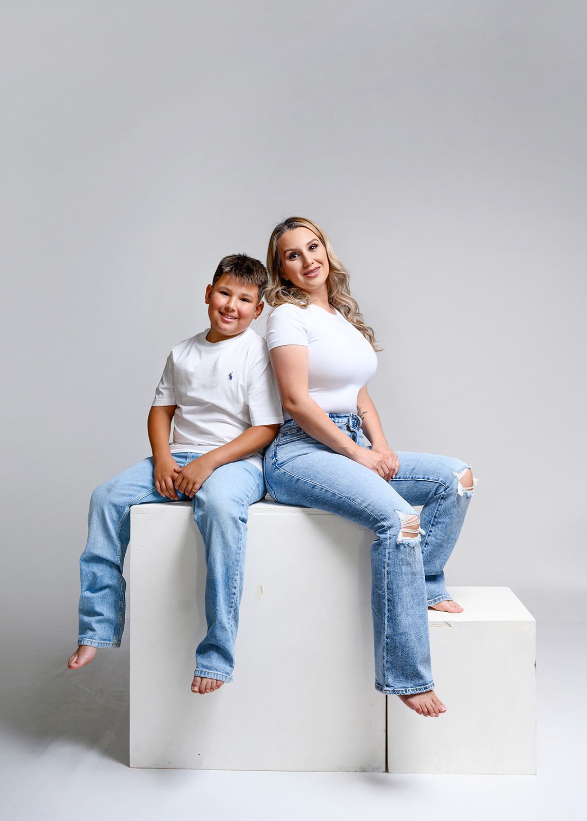 Two people in white shirts and jeans sit on white blocks against a gray background.