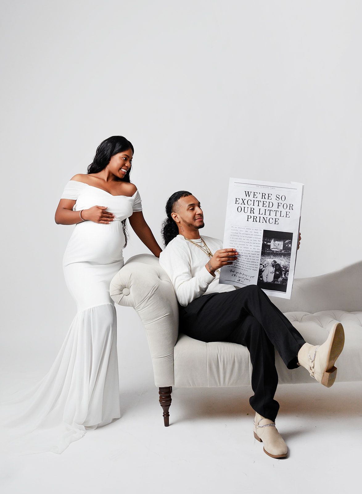 Three people in white and black outfits posing in a studio, one seated holding a design board.