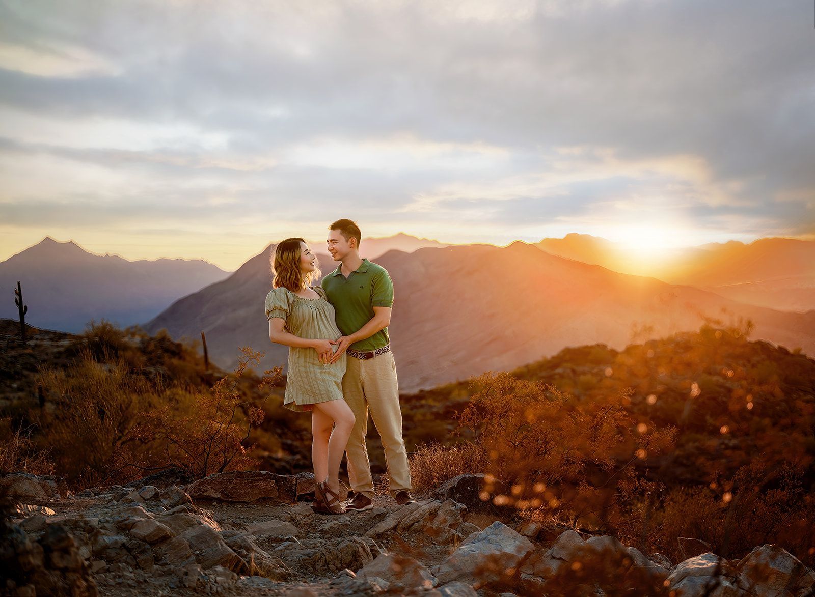 Couple standing on a rocky mountain at sunset, with golden light over distant peaks.