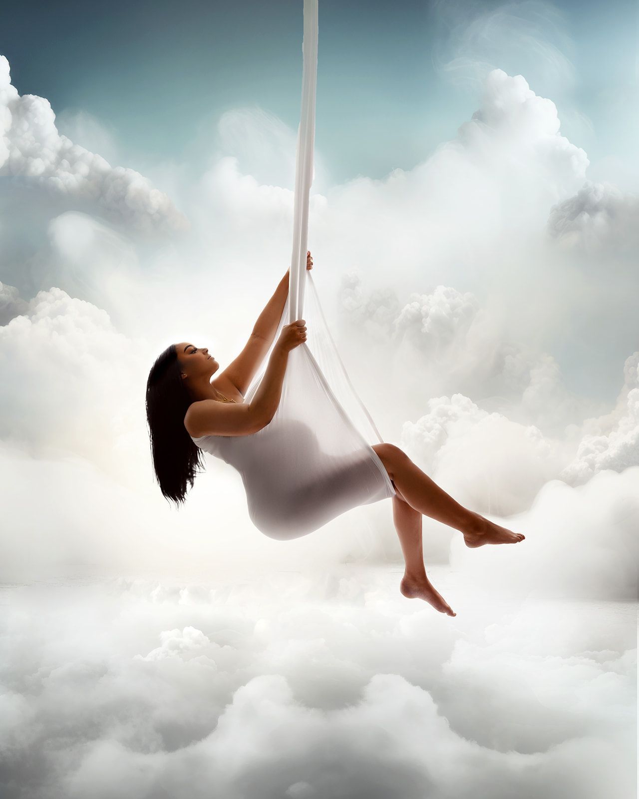 Woman in a white dress swinging on a rope above clouds under a bright sky