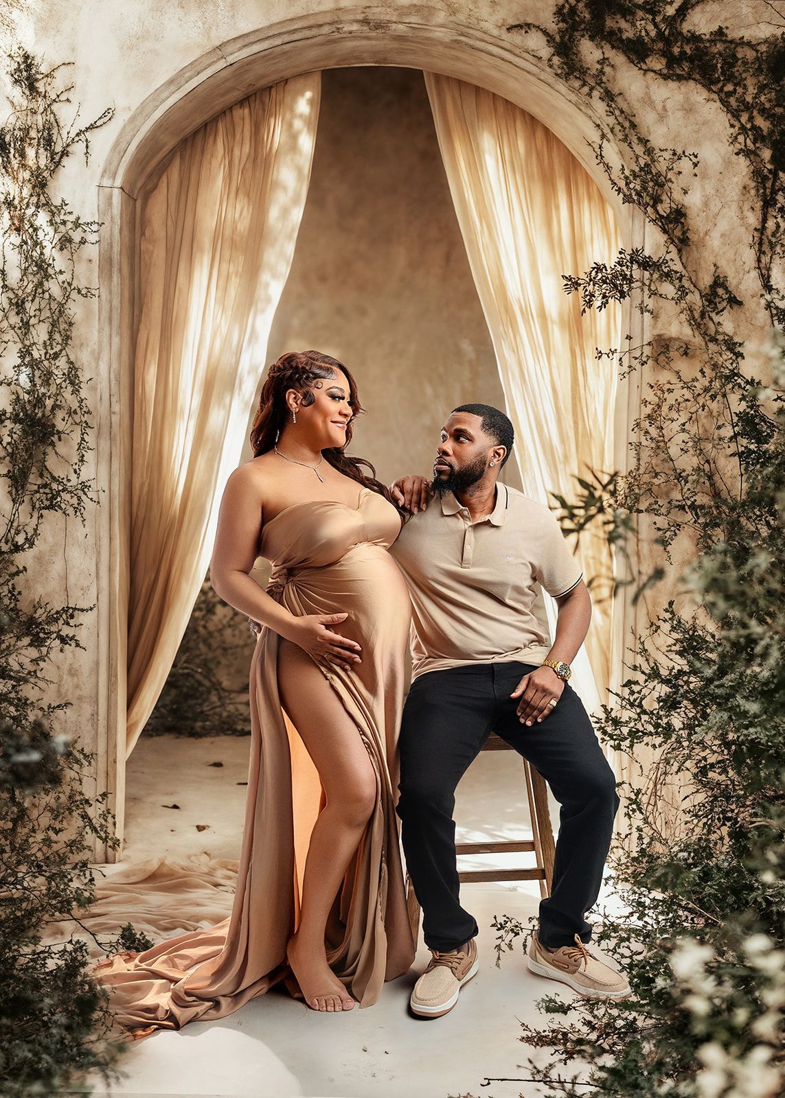 Couple posing in a rustic archway, with flowing beige drapery and greenery surrounding them.