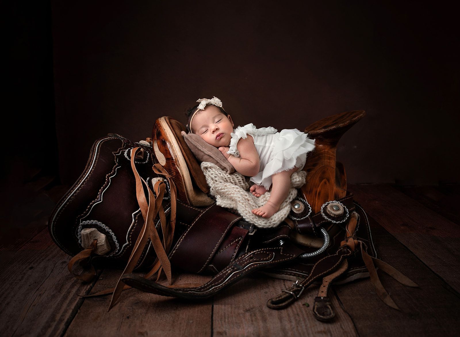 Sleeping baby in a white dress nestled in a rustic brown wooden cradle with leather straps.