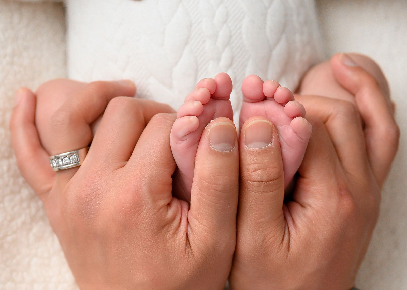 Adult hands gently holding newborn baby feet on a white blanket.