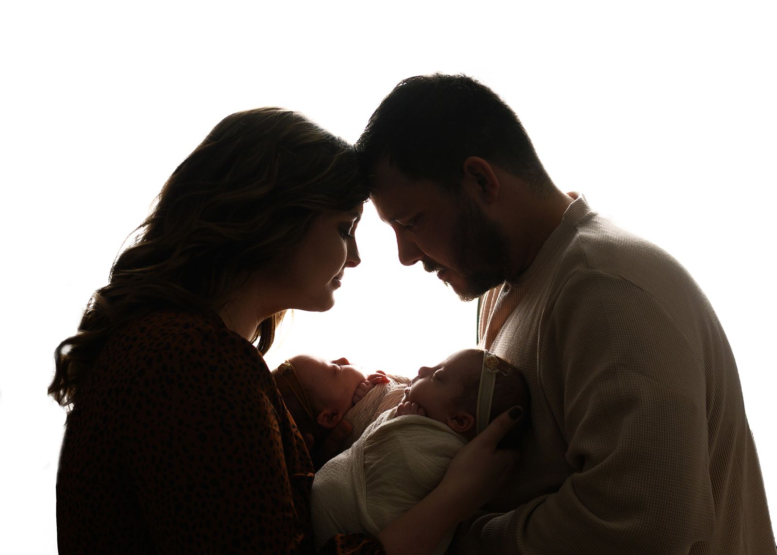 Silhouetted couple gently holding a newborn, facing each other against a bright white background.