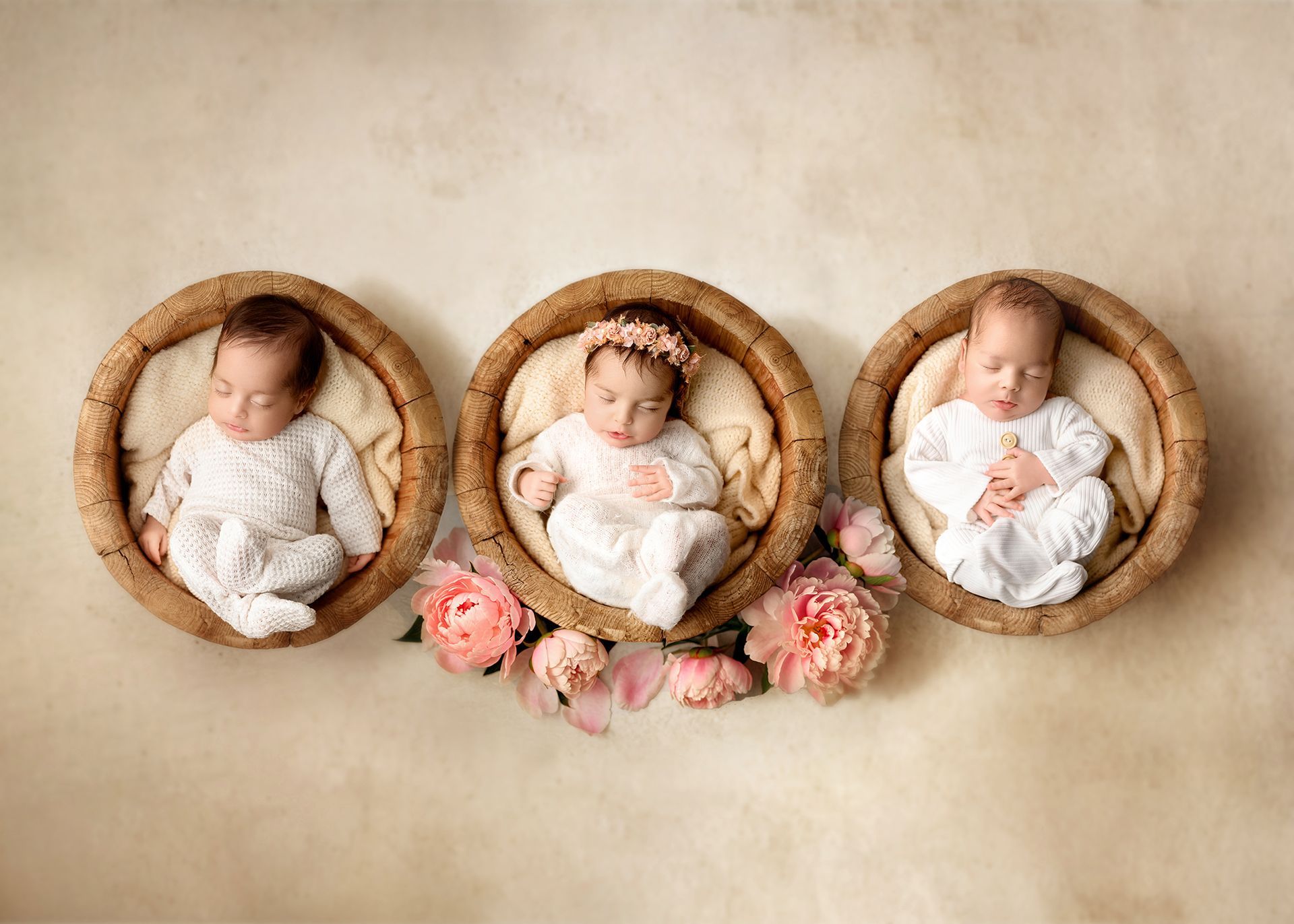 Three sleeping babies in woven baskets with pink flowers on a soft beige background.