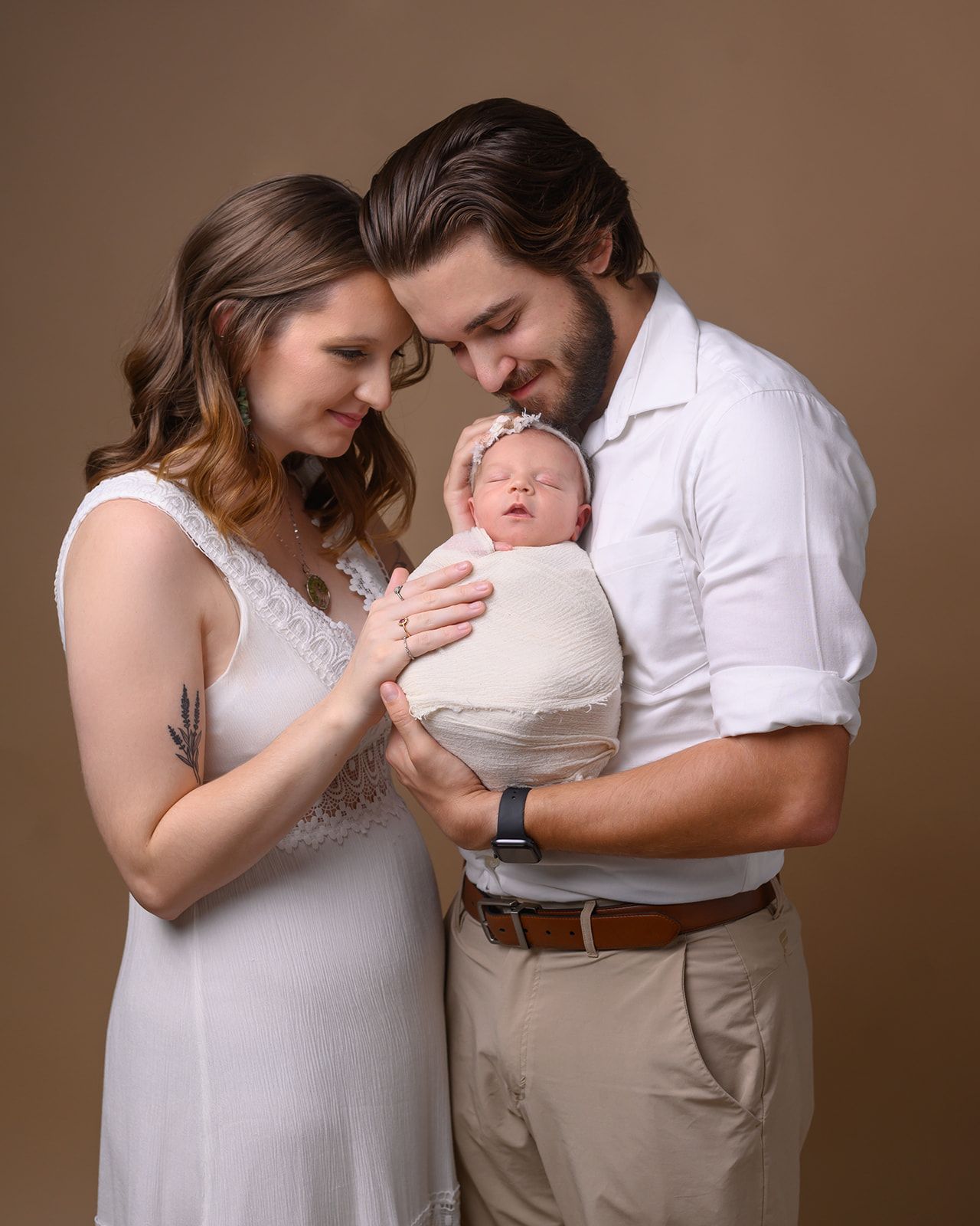 Parents holding a swaddled newborn in a warm studio portrait.