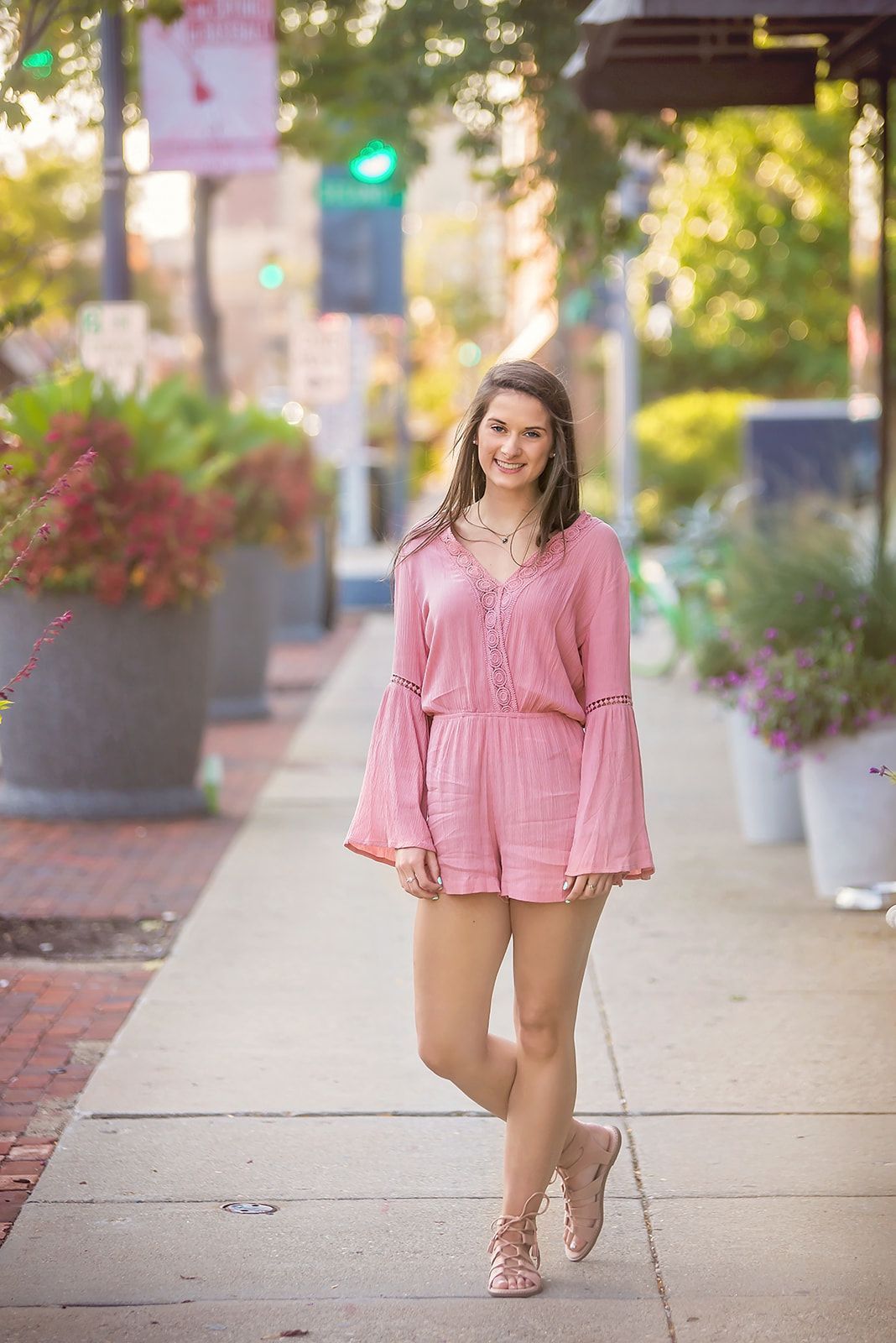 Woman in a pink dress walking on a sunny sidewalk with flower planters.