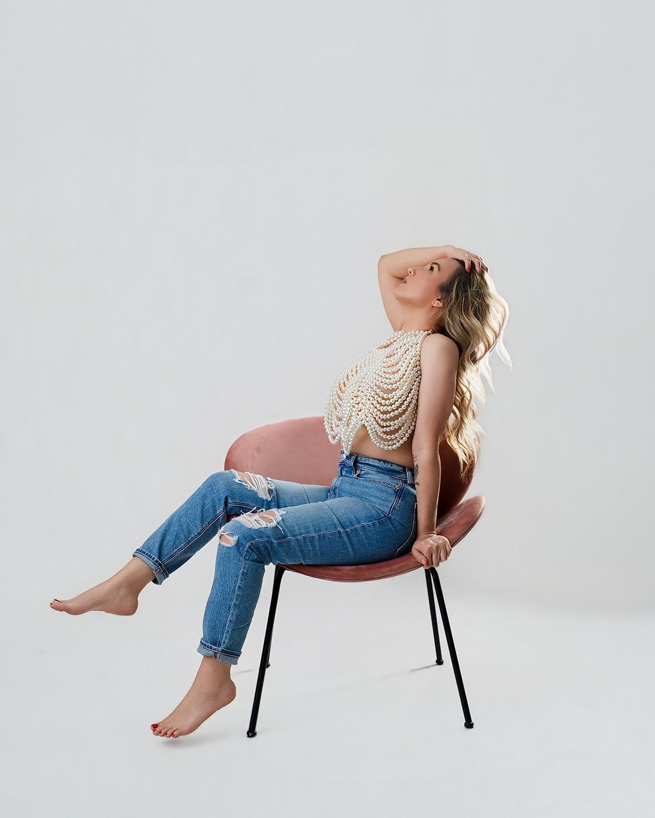 Pregnant woman reclining on a chair against a plain white background, wearing jeans and a patterned top.