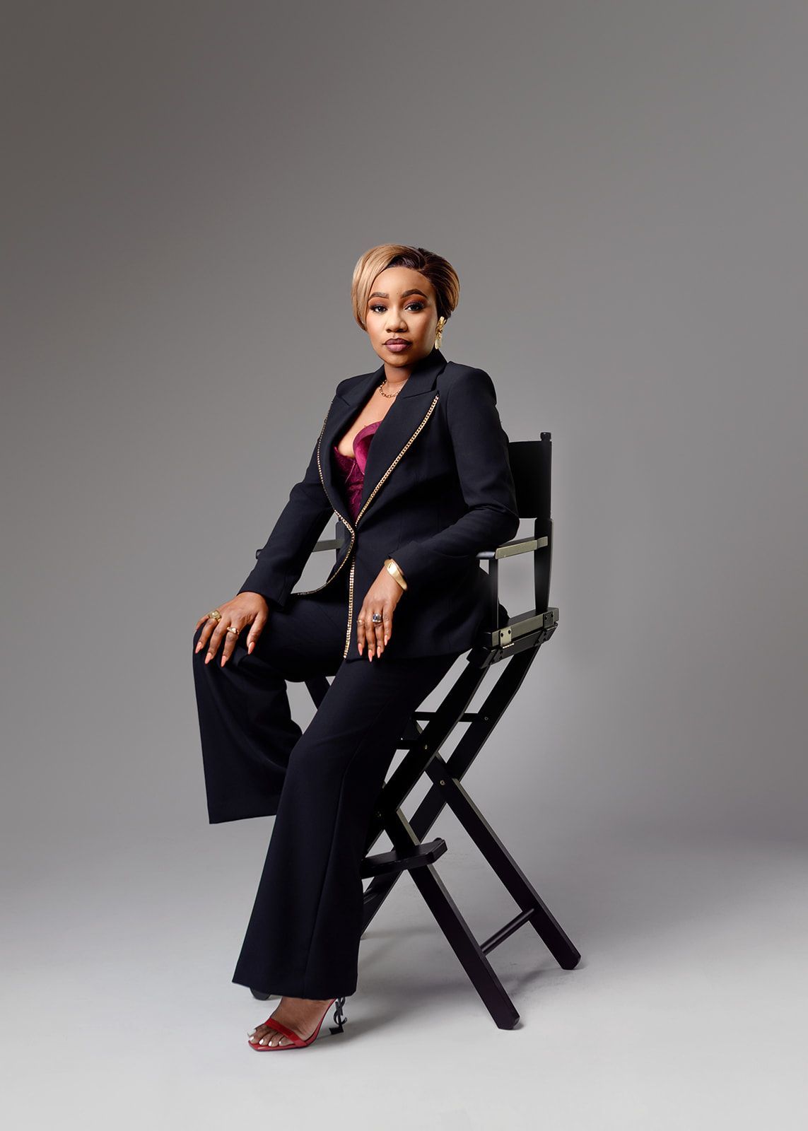 Woman in a navy suit seated on a black chair against a gray studio backdrop.