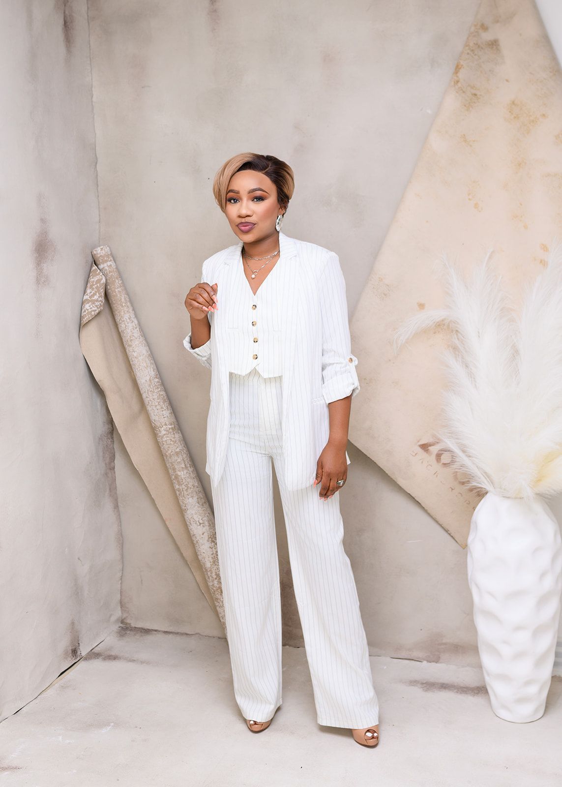 Woman in a white outfit posing in a minimalist beige studio with sculptural decor.