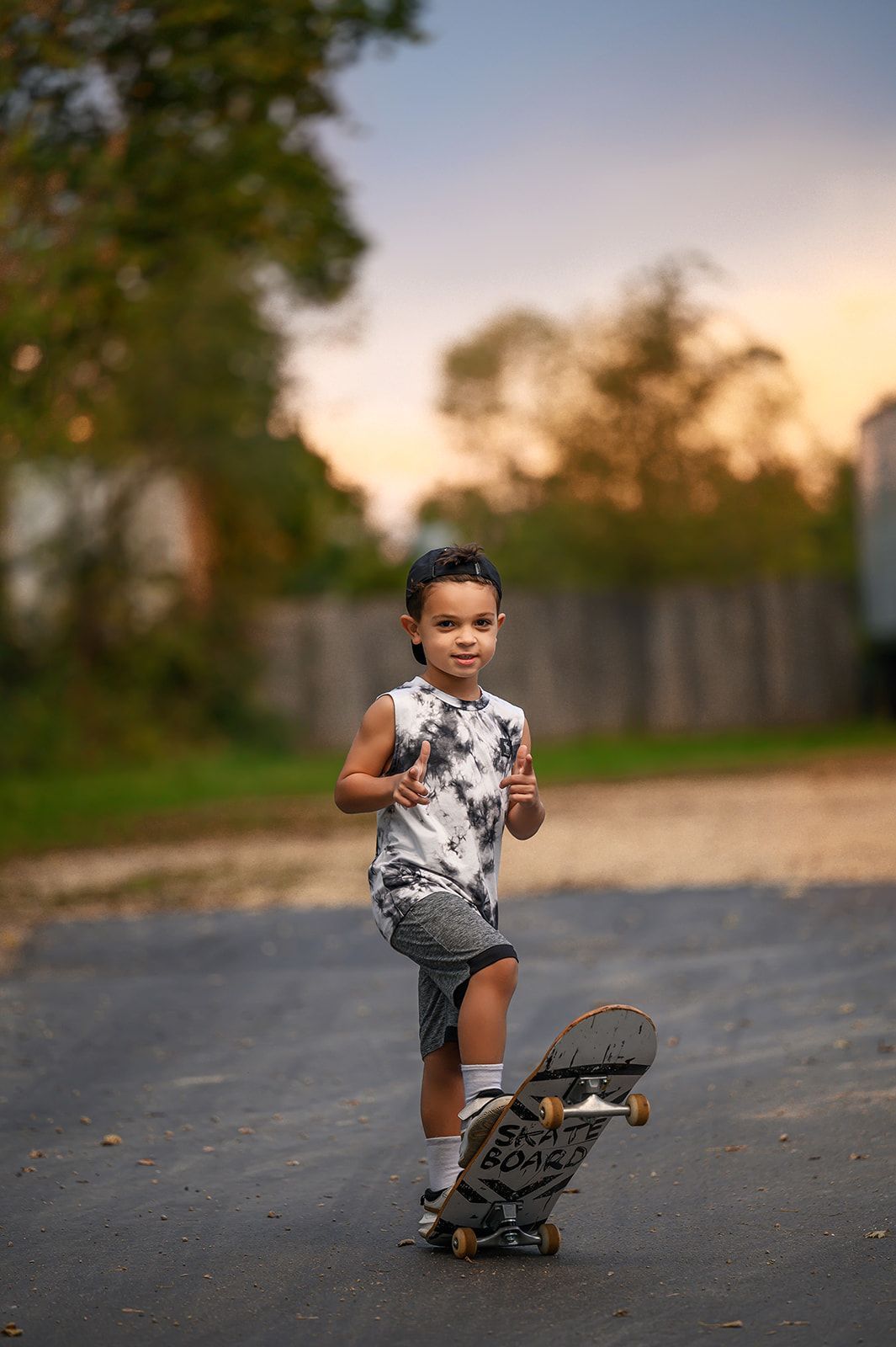Child on a skateboard on a road at sunset, running toward the camera with a blurred outdoor background.