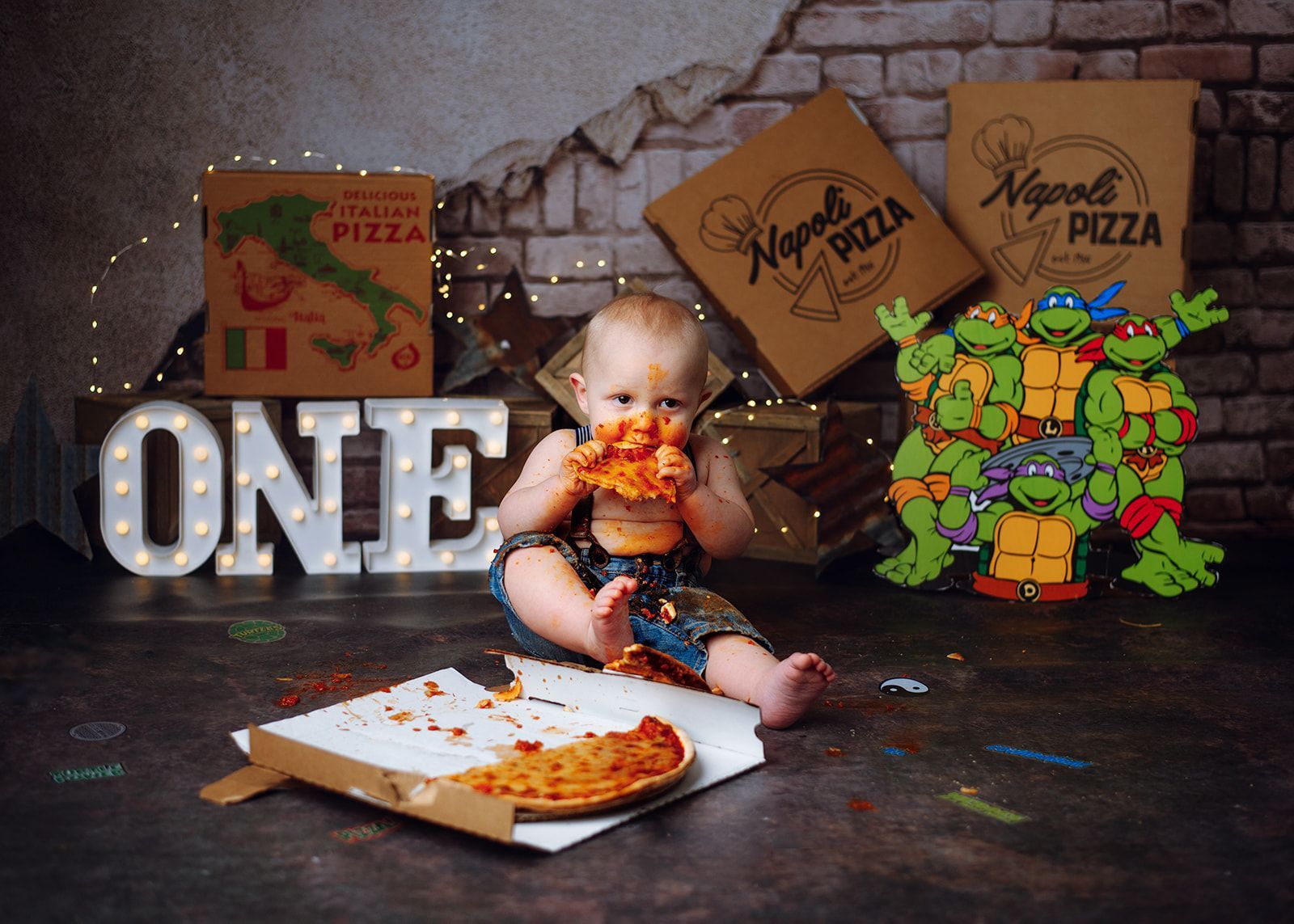 One-year birthday scene with a baby, pizza slices, and Teenage Mutant Ninja Turtles decorations.