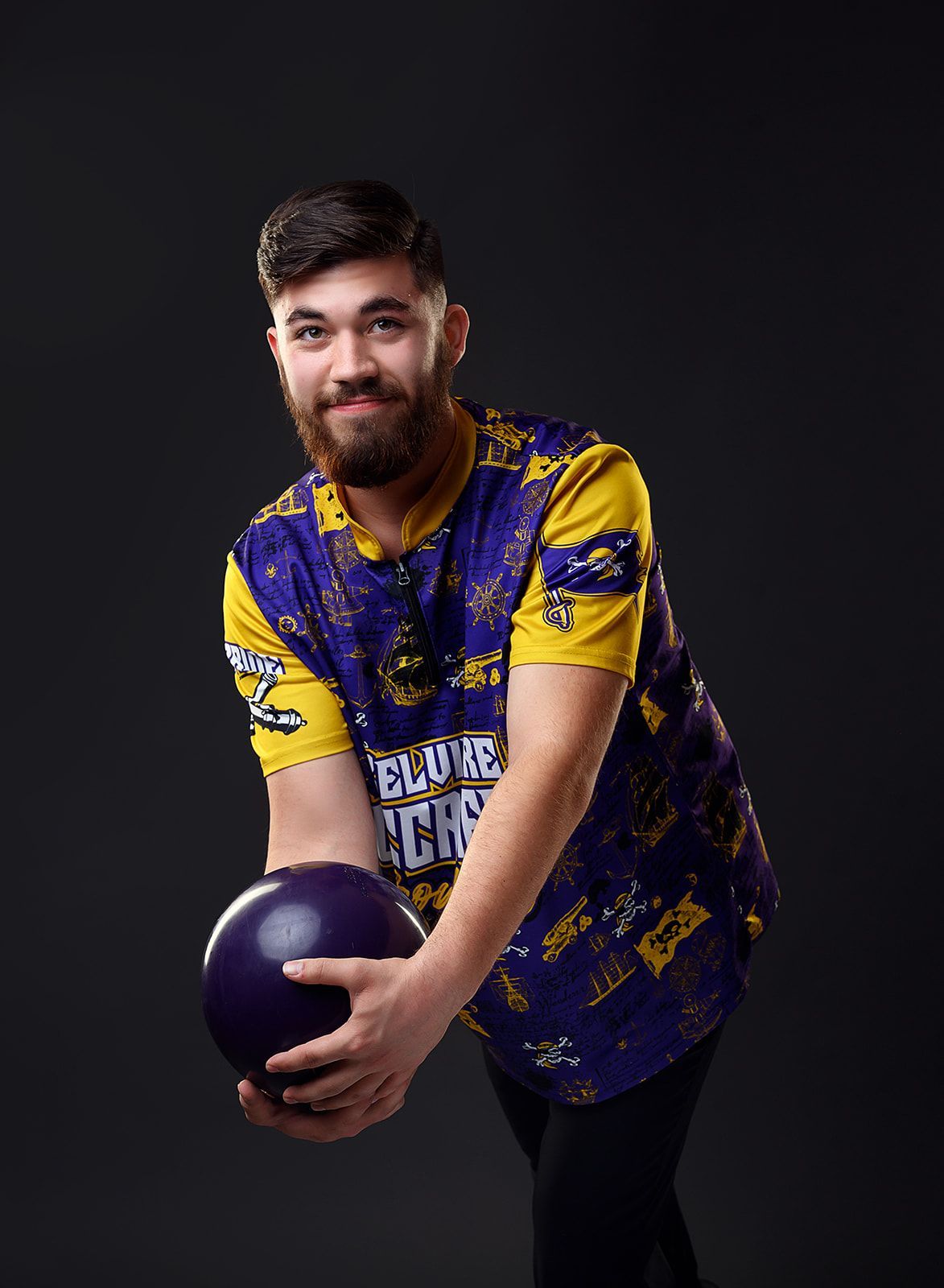 Man holding a bowling ball in a blue-and-yellow shirt against a dark background.