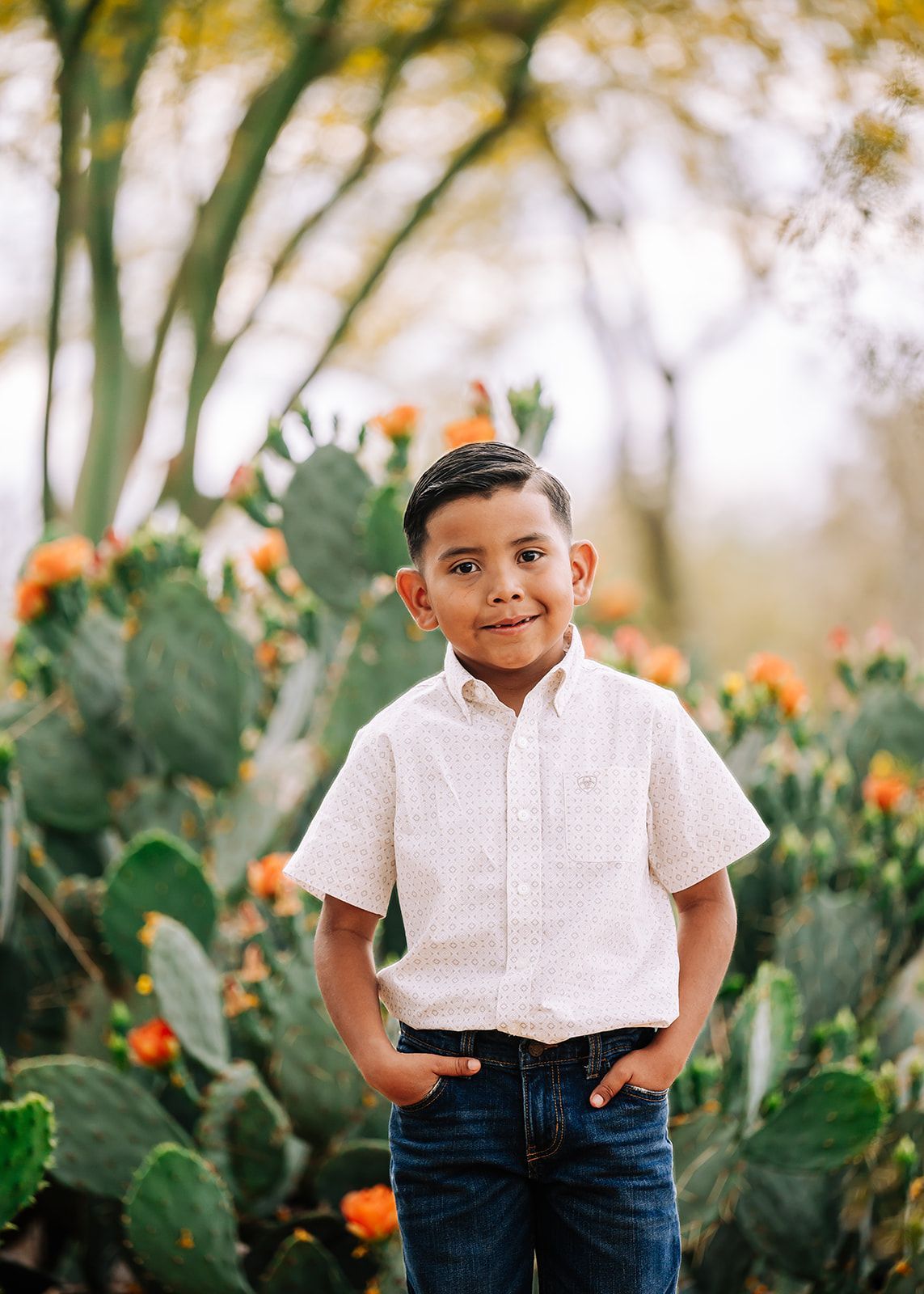 Smiling child standing in a cactus garden, wearing a white shirt and jeans.