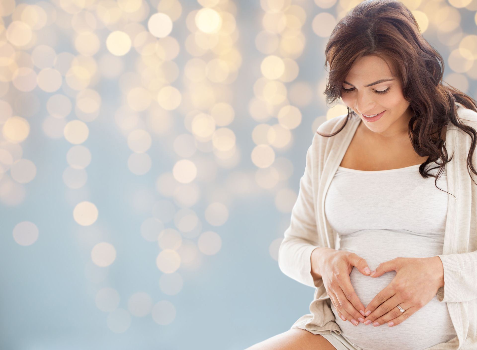 Woman in white sweater gently holding her pregnant belly against a soft, glowing background