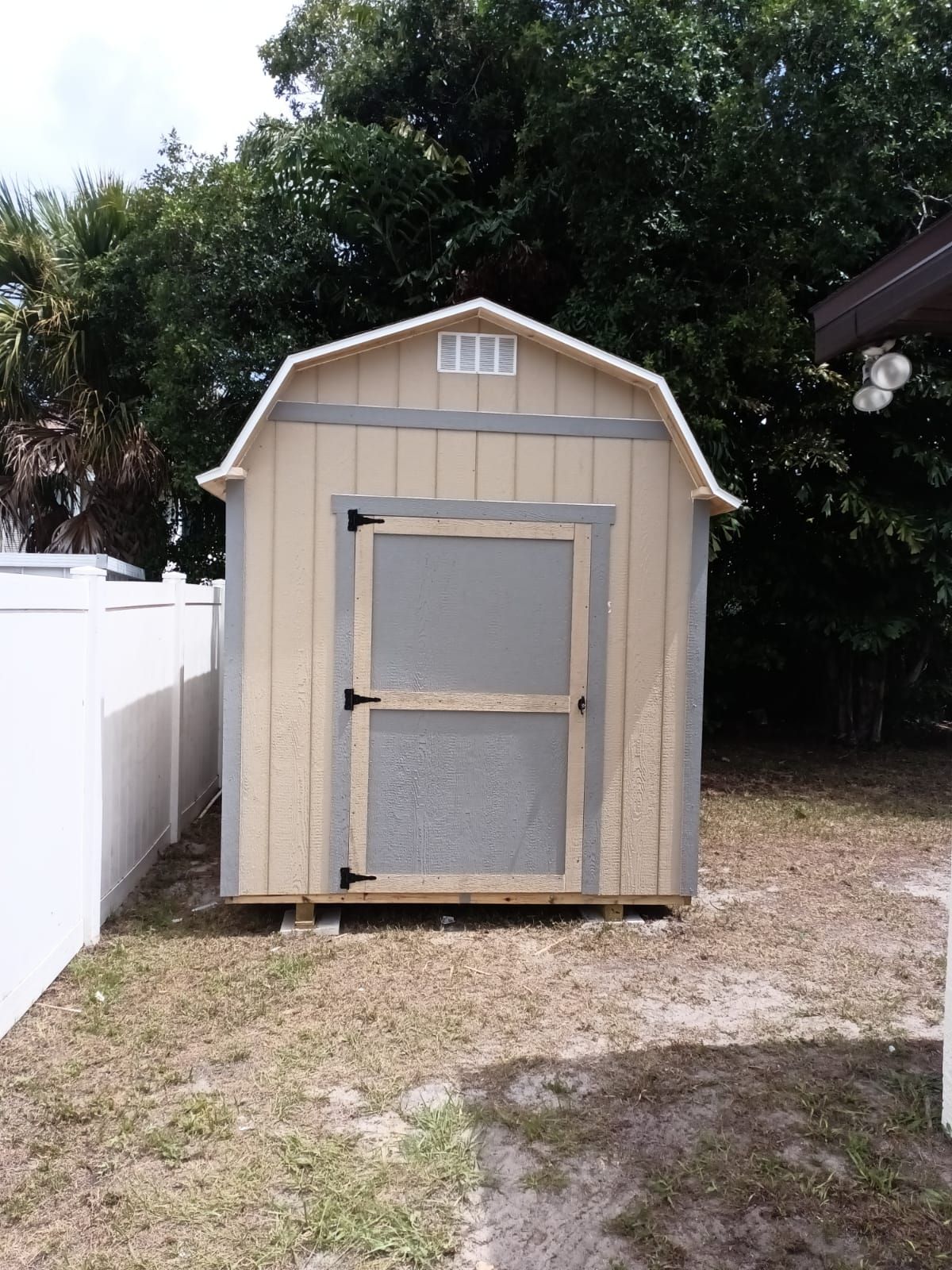 A small barn shed in a backyard next to a white fence