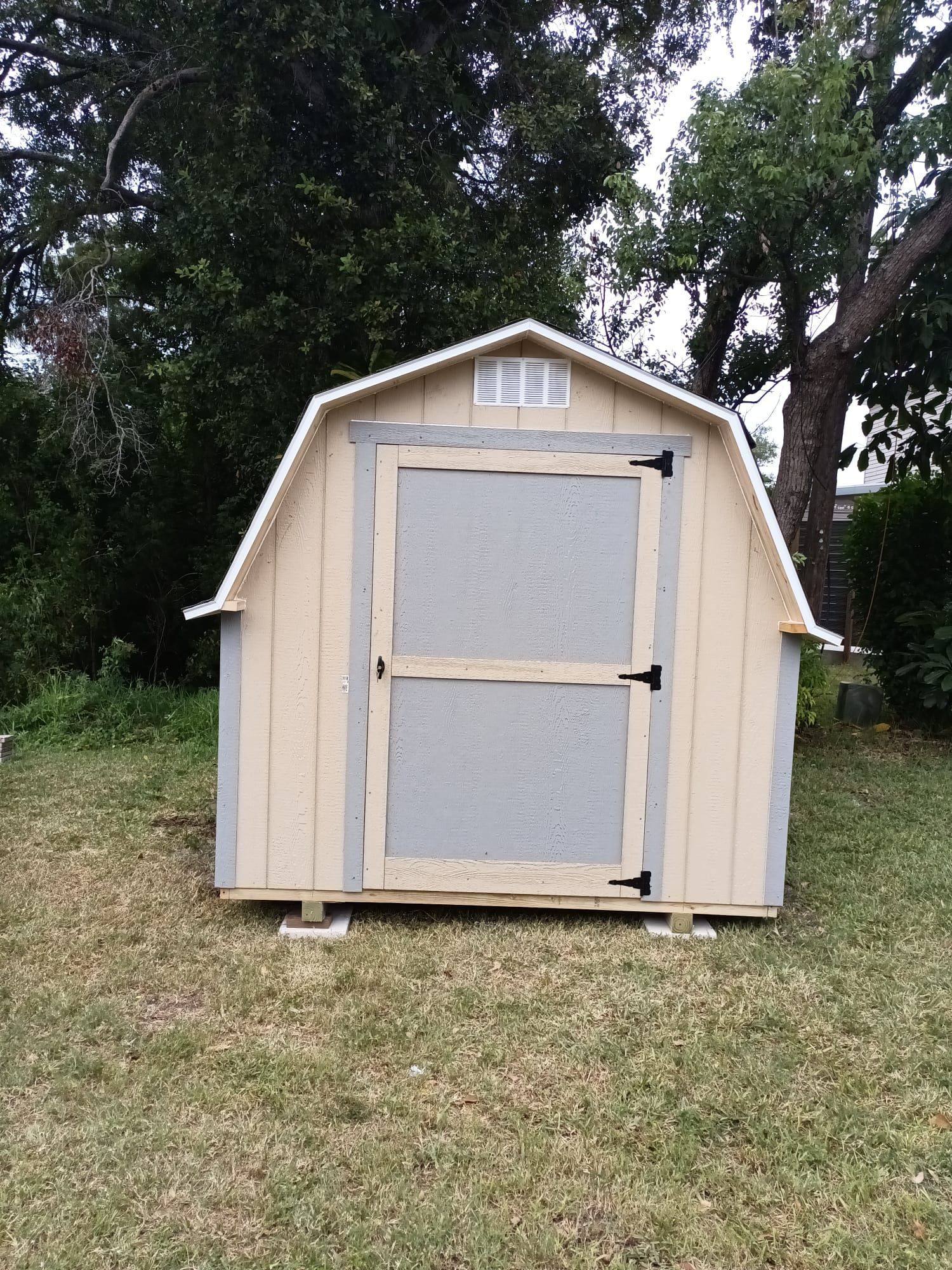 A small barn shed is sitting in the middle of a grassy yard