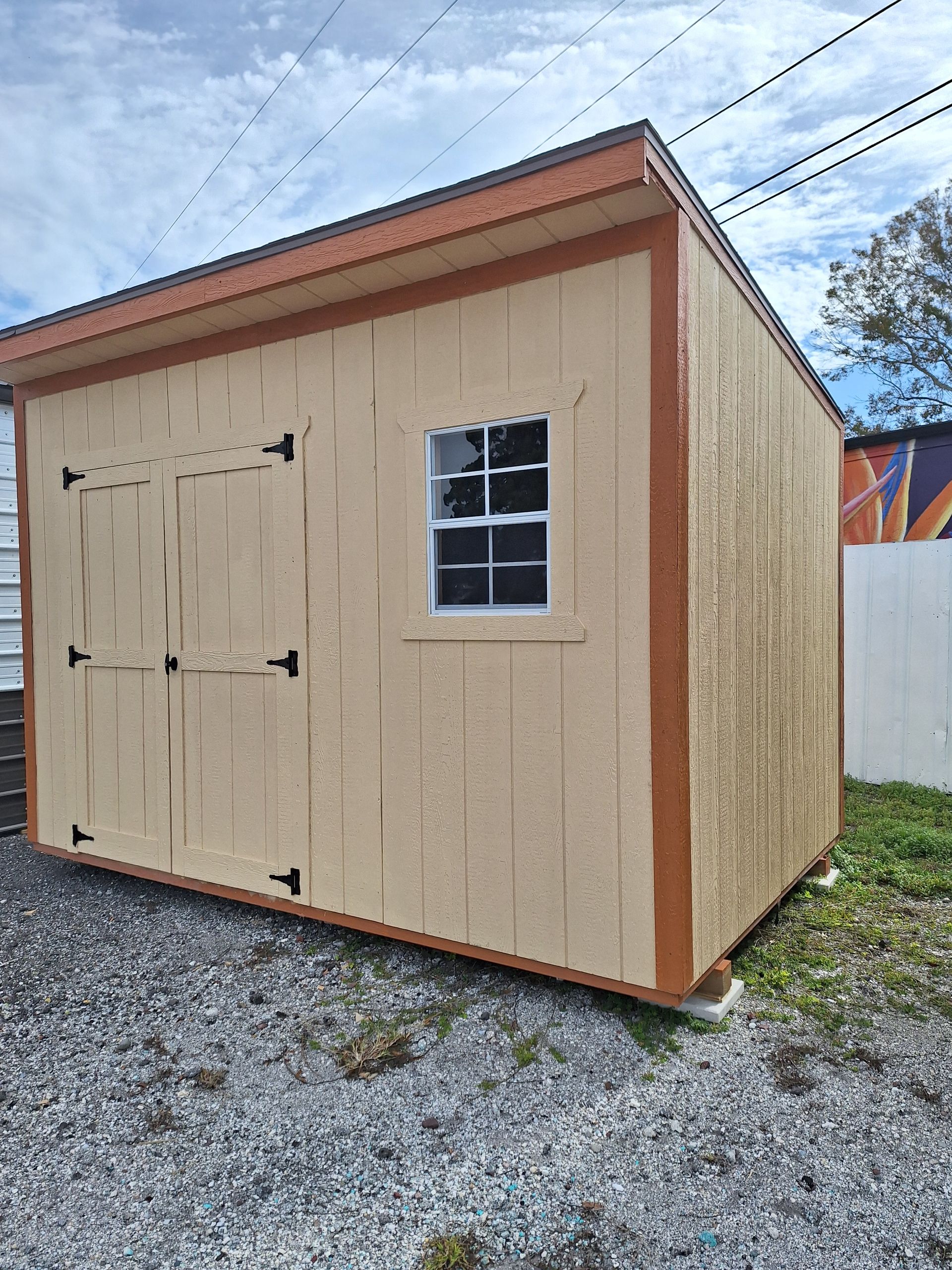 A small wooden shed with a window is sitting on top of a gravel lot