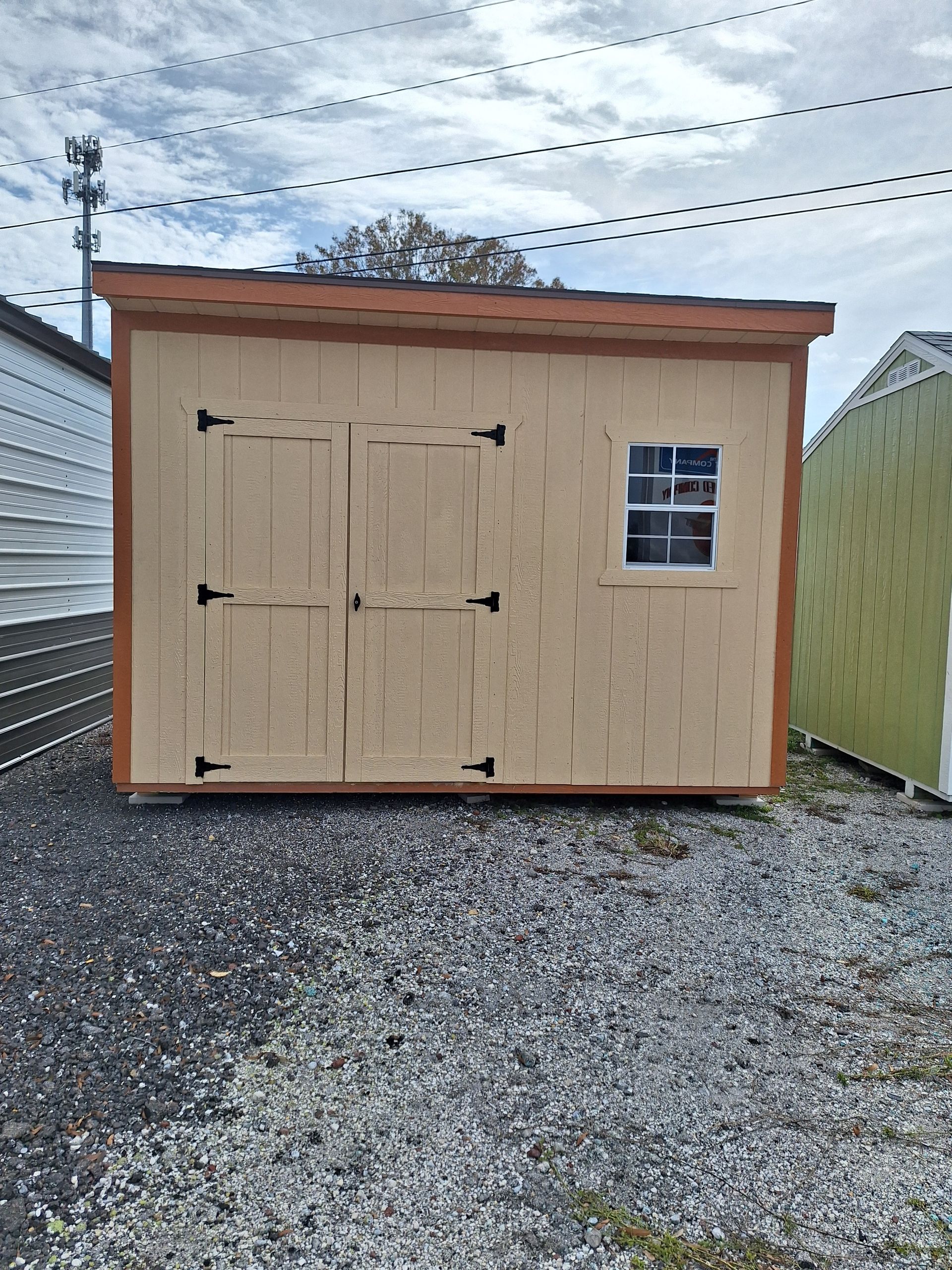 A wooden shed with a window is sitting on top of a gravel lot