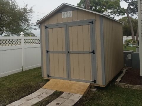A shed with a ramp attached to it is in the backyard of a house