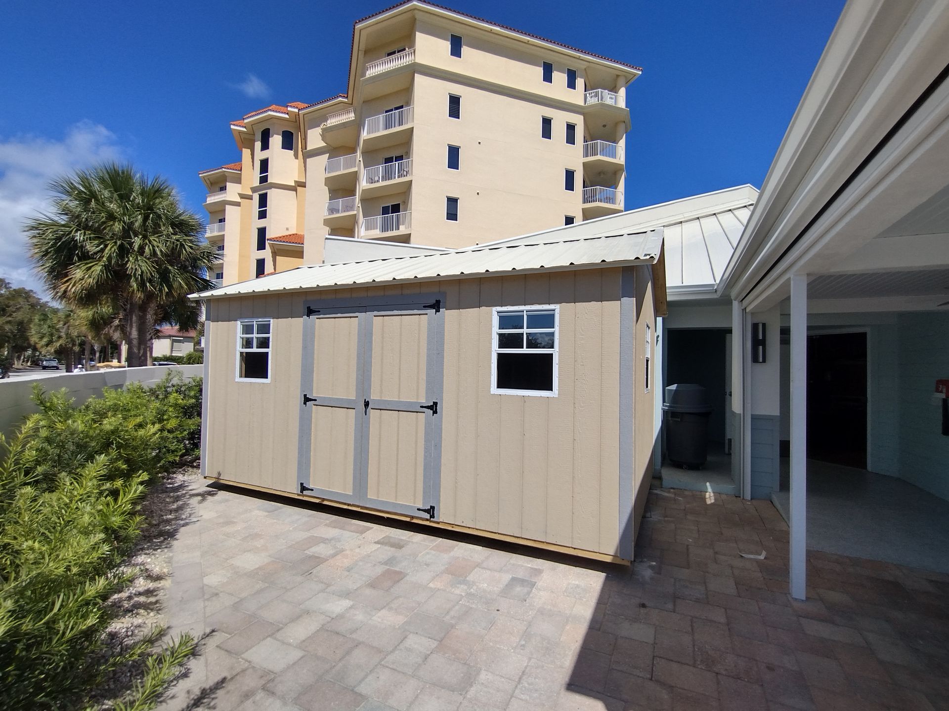 A tan shed with a white roof sits in front of a building
