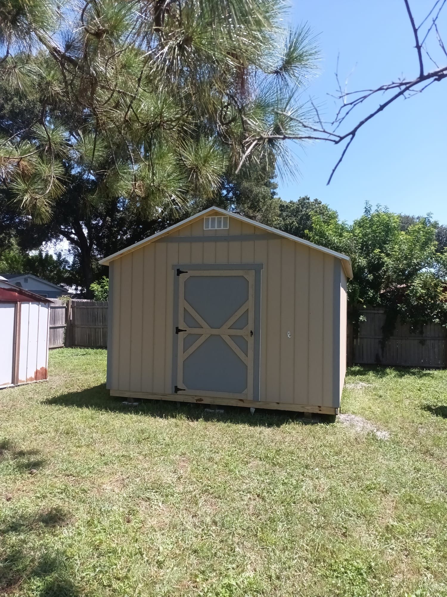 A small shed is sitting in the middle of a grassy yard.