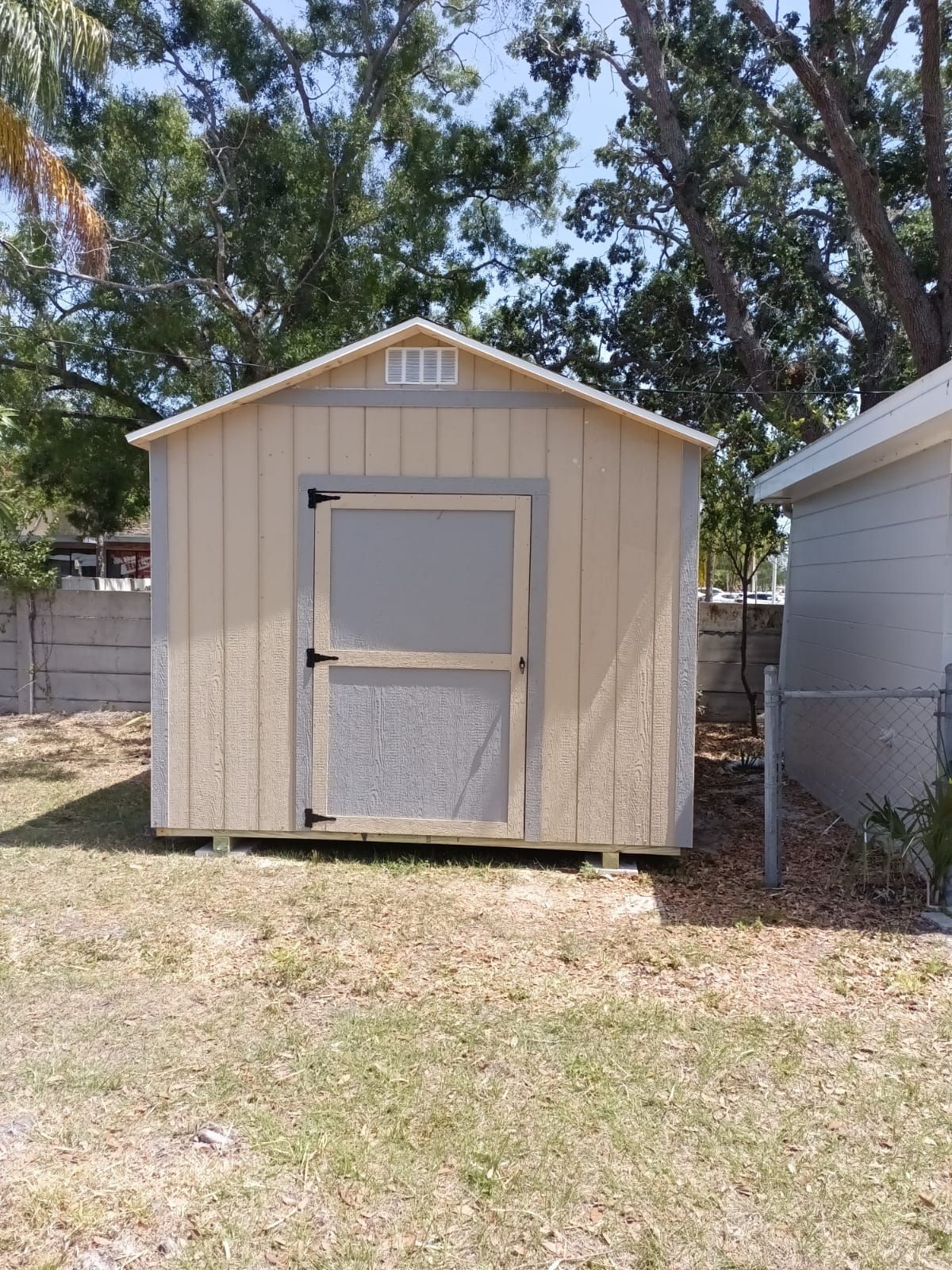 A small shed is sitting in the middle of a grassy yard next to a house.