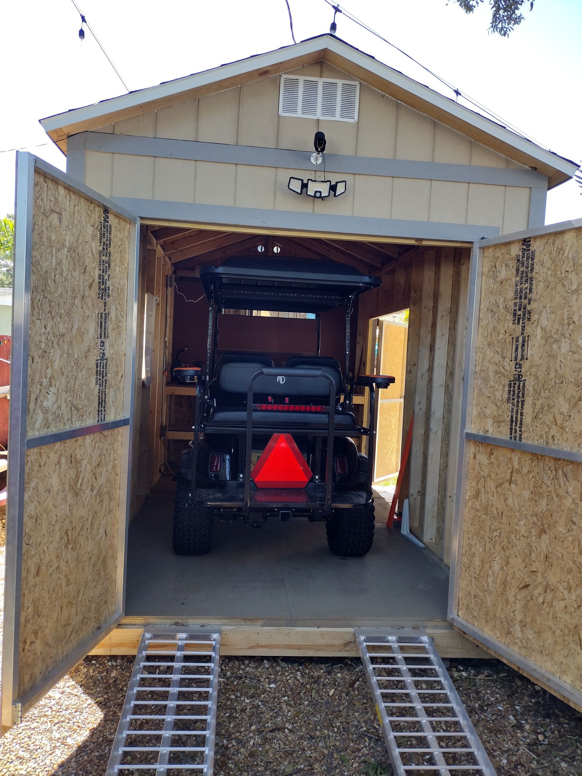 A golf cart is parked in a shed with the doors open