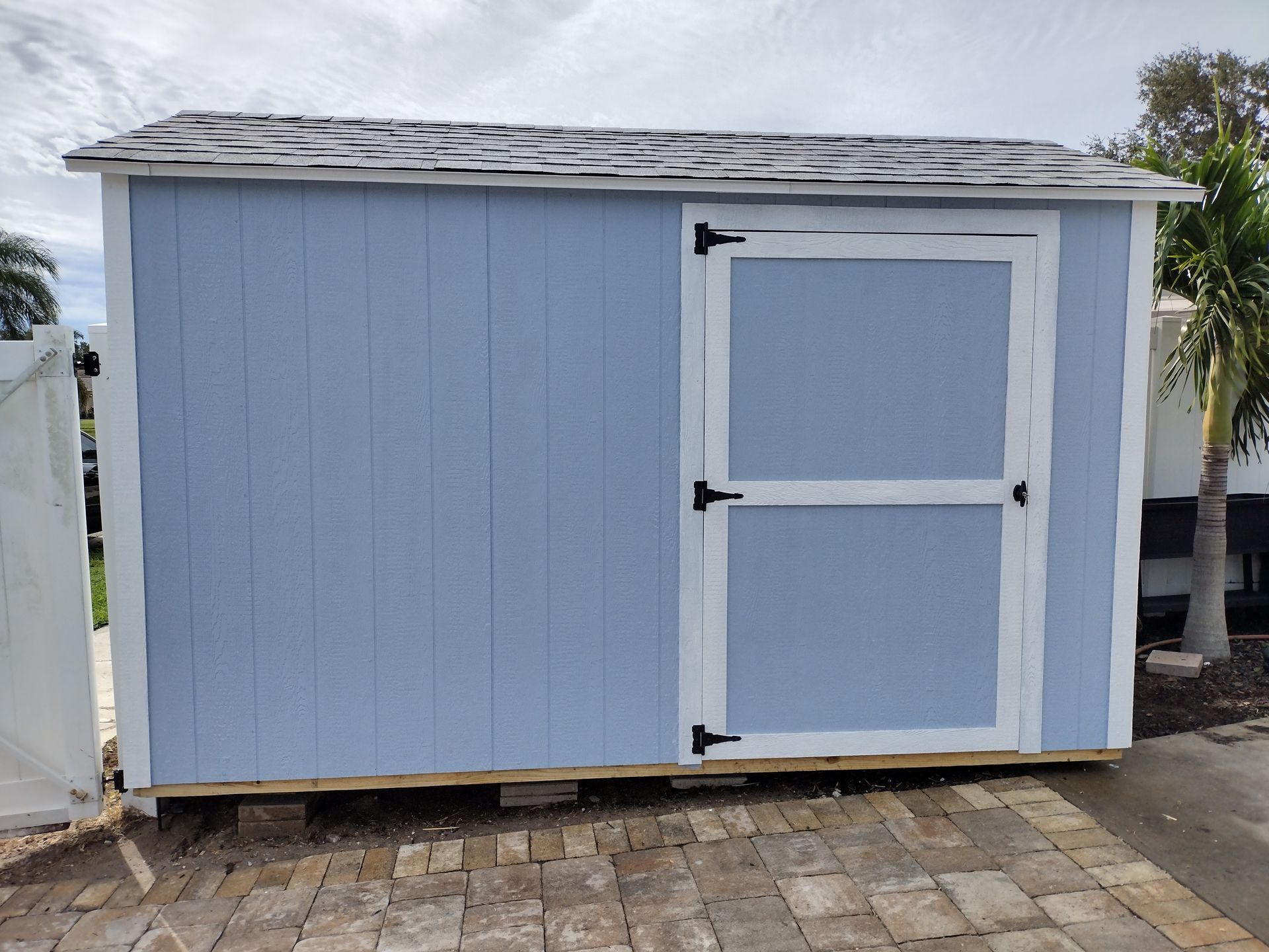 A blue and white shed is sitting on a brick driveway.