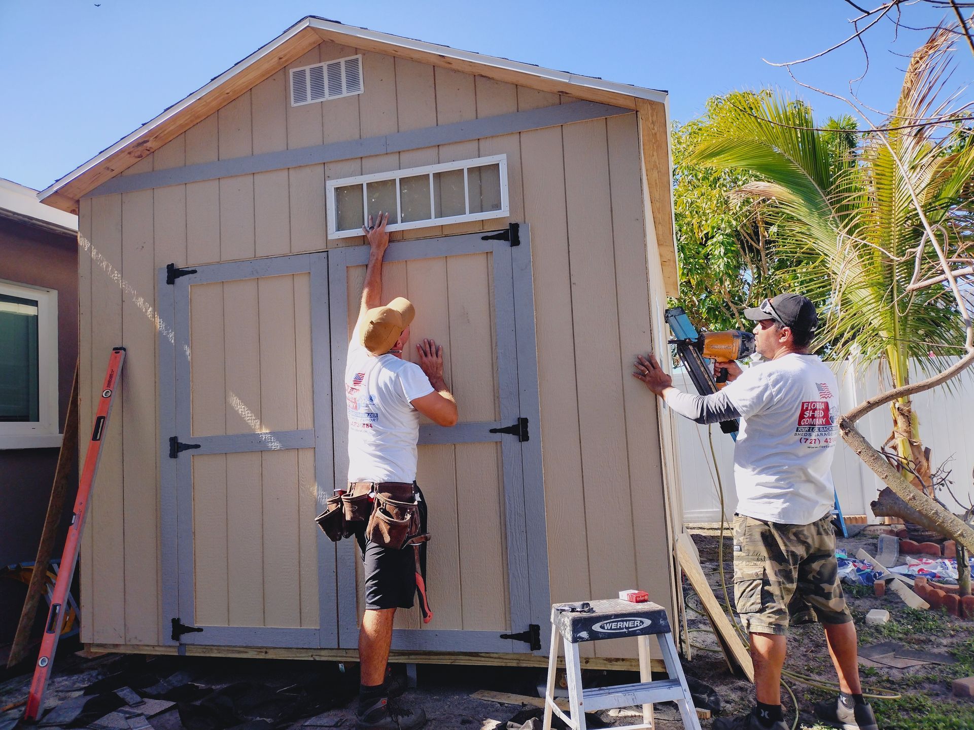 Two men are working on a shed in a backyard.