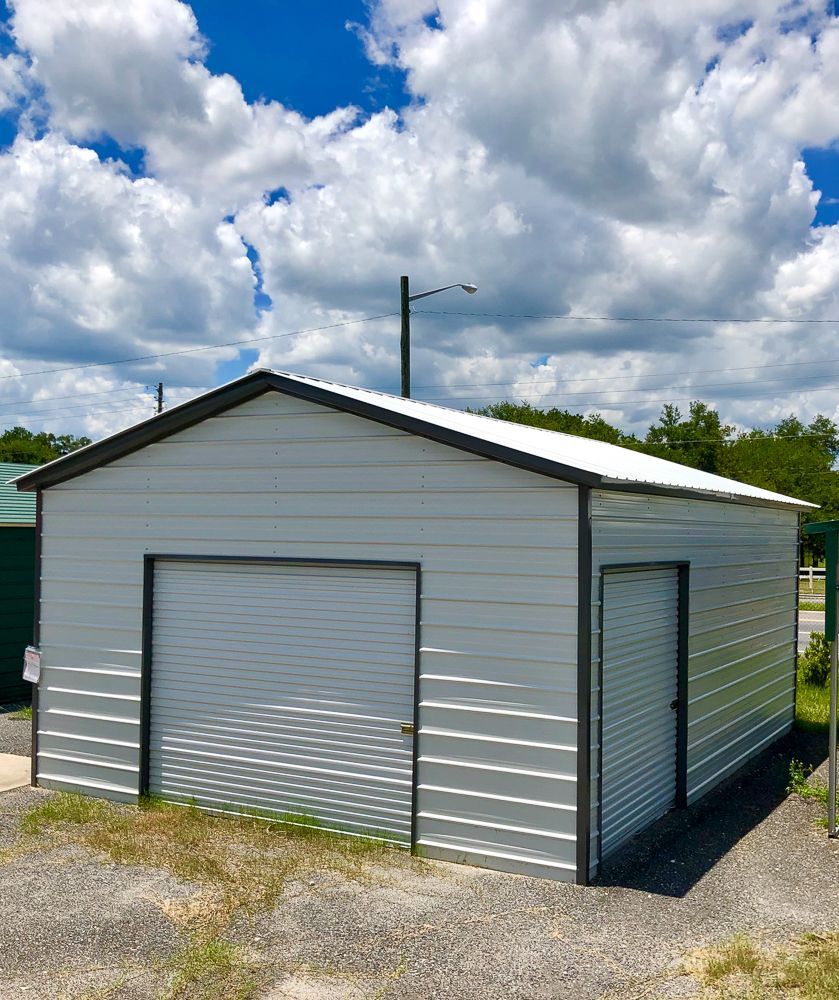 A white garage with a black roof is sitting in the middle of a dirt field.