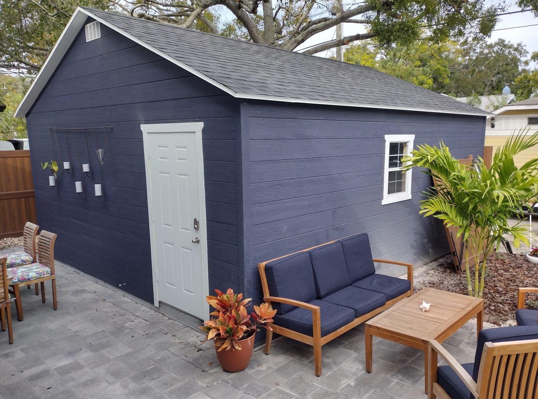 A blue shed with a couch, table and chairs in front of it.