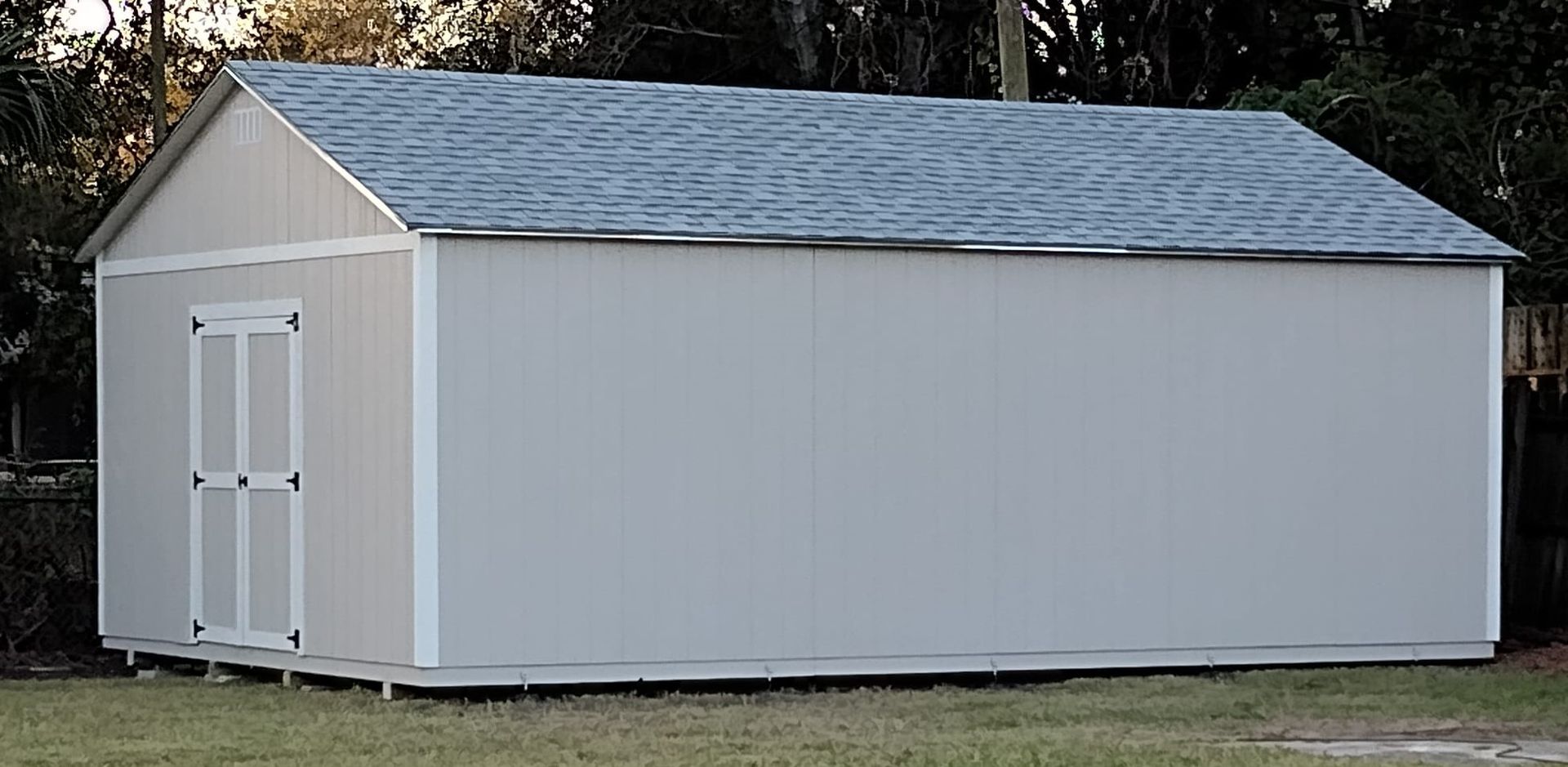 A white shed with a blue roof is sitting in the grass.