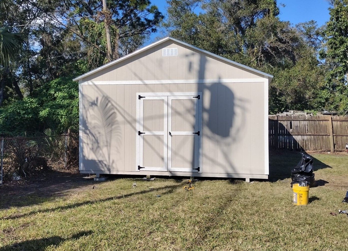 A small shed is sitting in the grass next to a fence.