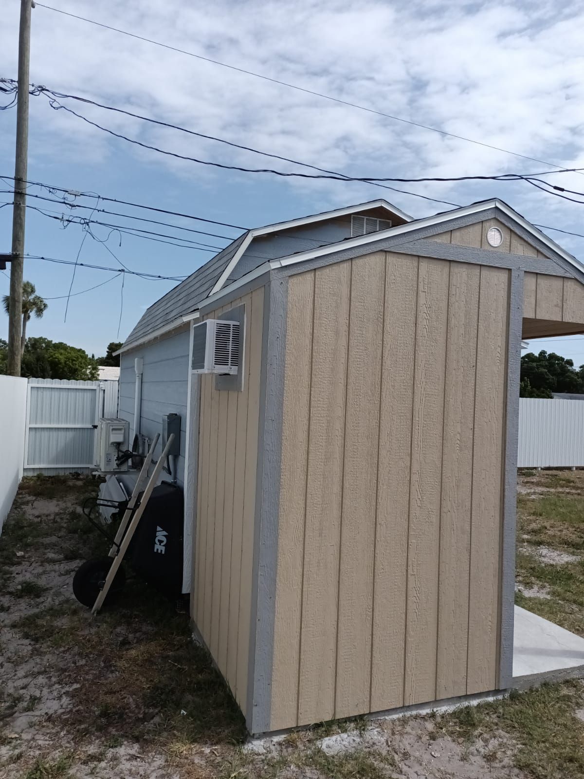 A small shed with a fan on the side of it in a backyard.