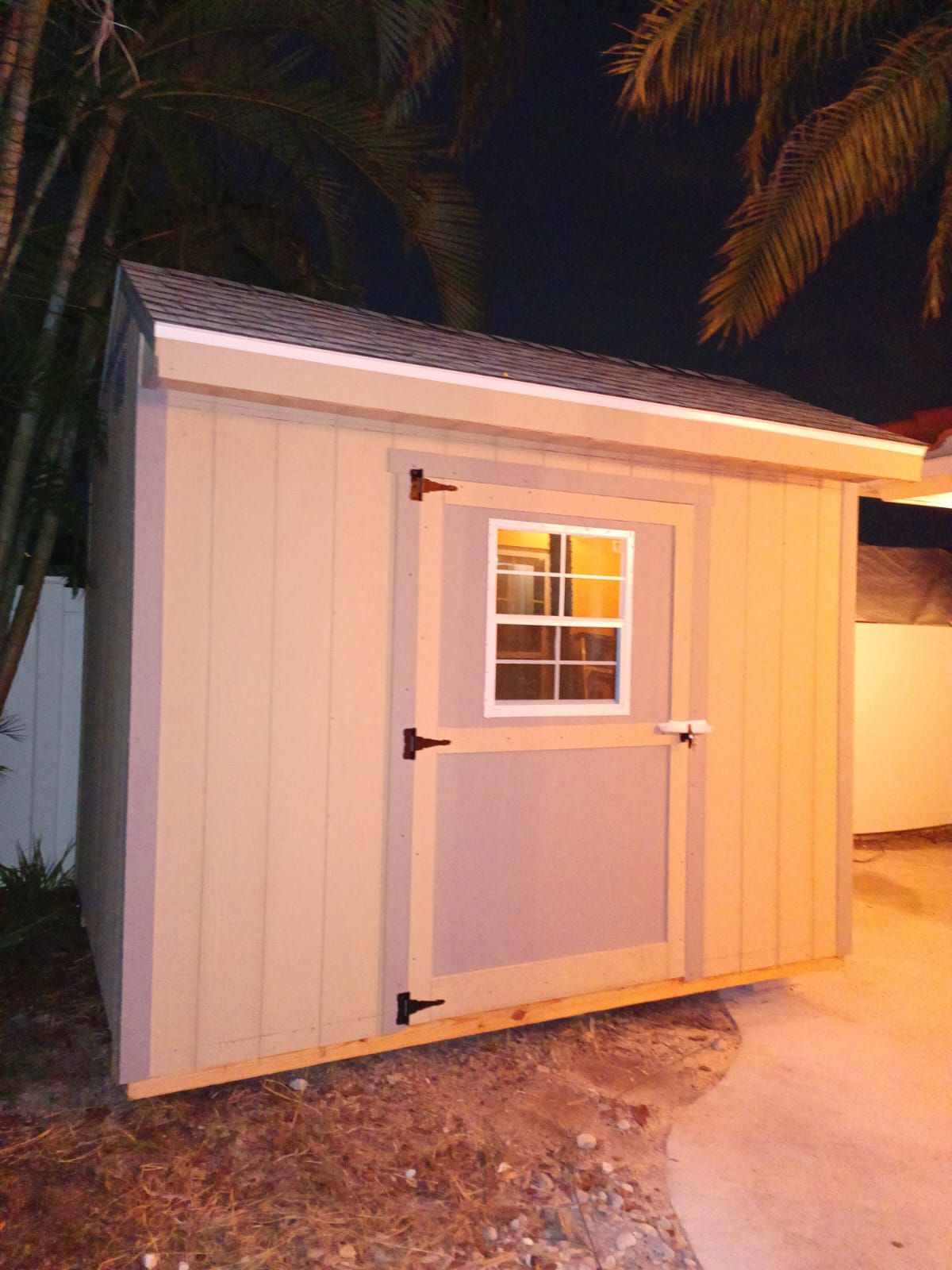 A shed with a window and a door is lit up at night.
