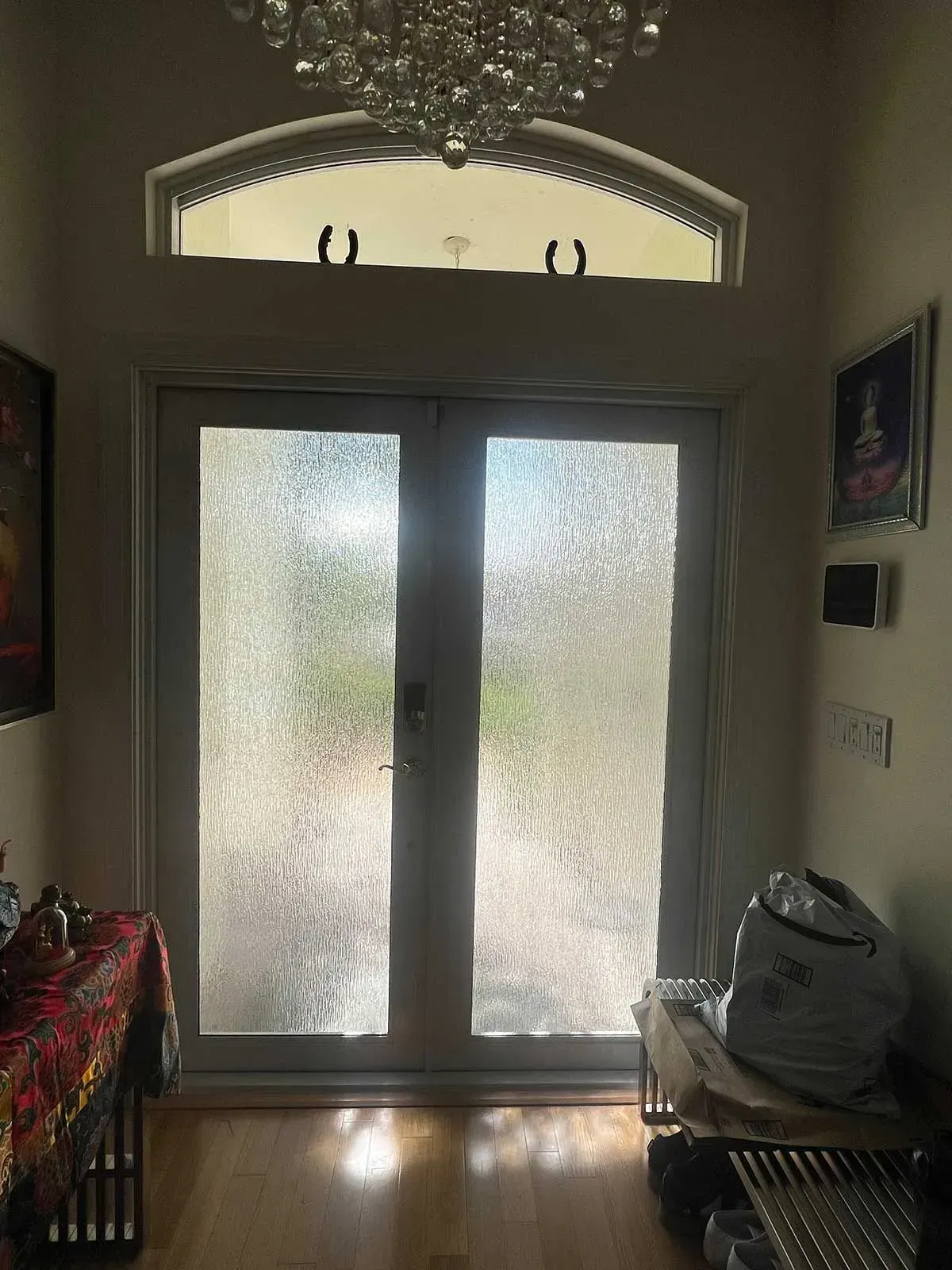 Two frosted-glass doors lead outside, with a chandelier above. The interior has wood floors and artwork.