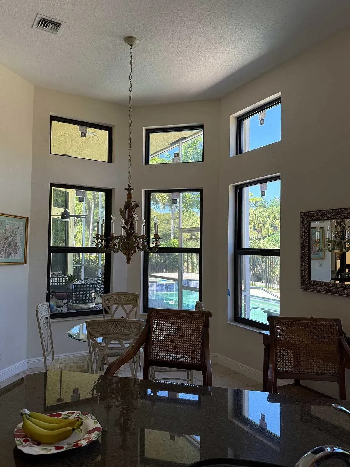 Interior view of a room with several windows overlooking a pool. A chandelier hangs in the center.